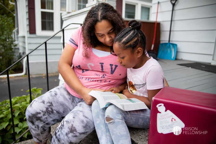 A woman and girl read together beside an Angel Tree Christmas gift.
